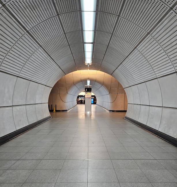 Inside the spacious concourse of Earls Court station, the image shows a modern, well-lit environment with large glass walls allowing natural light to flood in. Several passengers are walking across th
